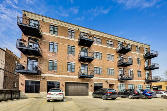 Front view of a multi-story apartment building with balconies and parking area.