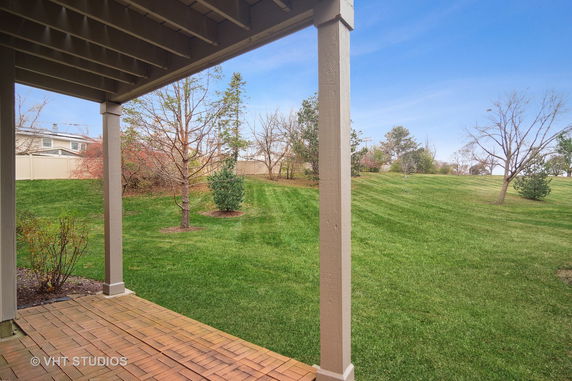 View from under a house porch overlooking a grassy lawn with scattered trees.