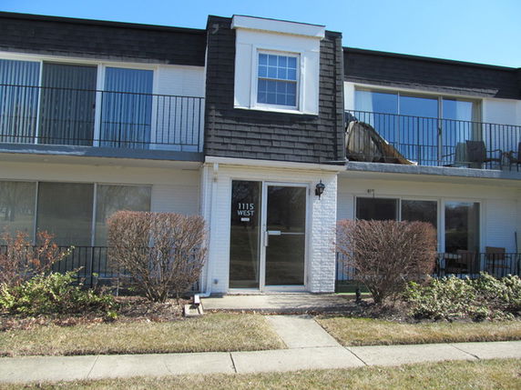 Front view of a multi-story building with balcony and sliding glass doors.