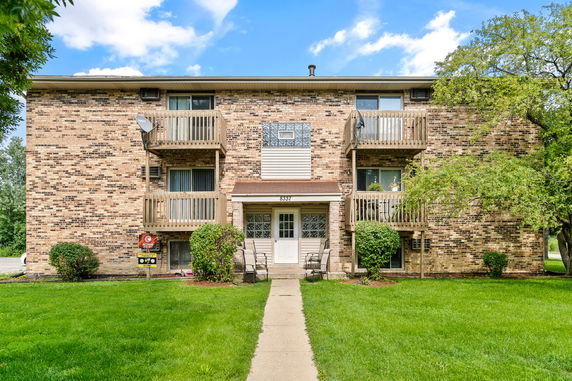 Front view of a three-story brick apartment building with balconies and a central entrance.