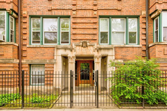 Front view of a brick building with decorative entrance and iron fence.
