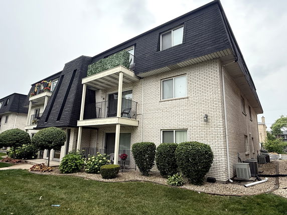 Front view of a three-story apartment building with balconies and a sloped roof.