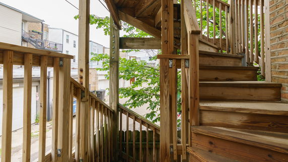 View of outdoor wooden staircase with railing leading up, buildings visible in the background.