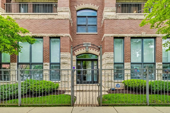 Front view of a multi-story brick building with large windows and a gated entrance.