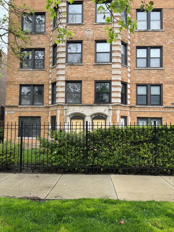 Front view of a multi-story brick building with multiple windows and a gated entrance.