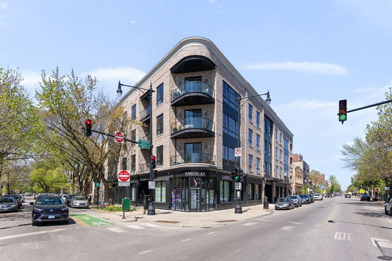 Front view of a multi-story brick building with balconies and large windows at a street corner.