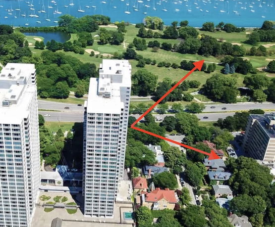 Aerial view of two tall buildings overlooking a green area and a body of water with many boats.