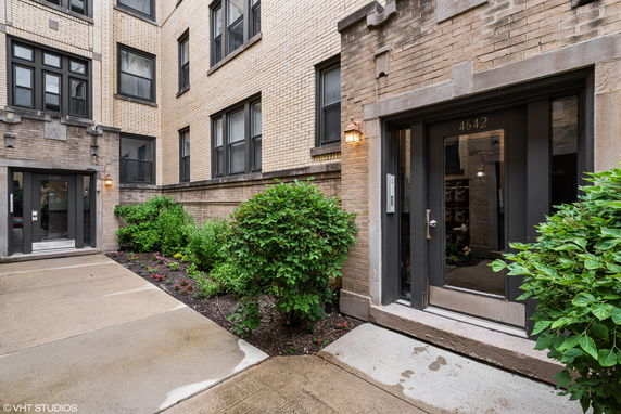 Front view of a multi-story brick building with two entrances and surrounding greenery.