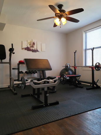 Room with exercise equipment including a bench press and barbells.