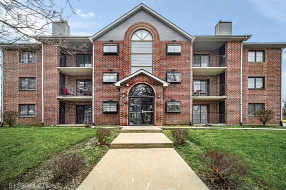 Front view of a brick multi-story apartment building with balconies.