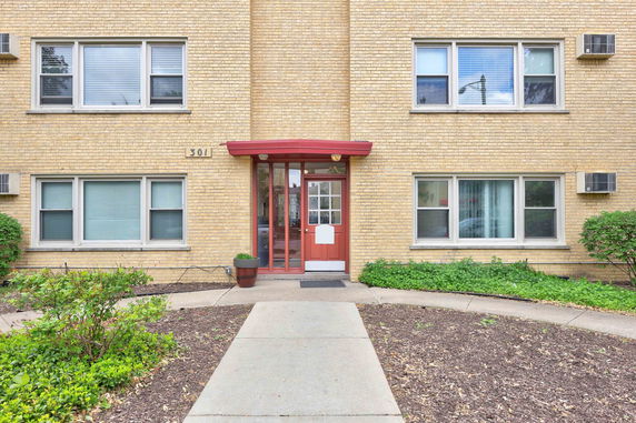 Front view of a building with a red entrance door and beige brick facade.