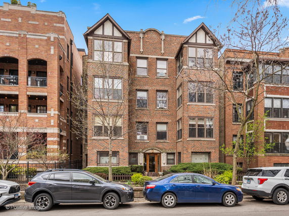 Front view of a multi-story brick building with cars parked in front.