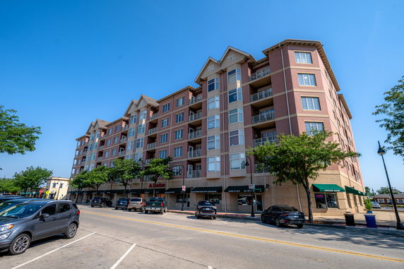 Front view of a multi-story apartment building with balconies and ground-level storefronts.
