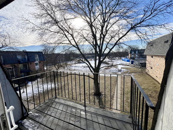 View from a building balcony showing neighboring buildings, a tree, and a grassy area with some snow.