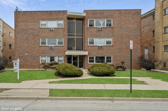 Front view of a three-story brick apartment building with large central windows.