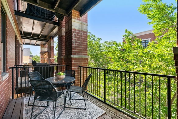 Outdoor balcony with a table and chairs offering a view of surrounding buildings and trees.