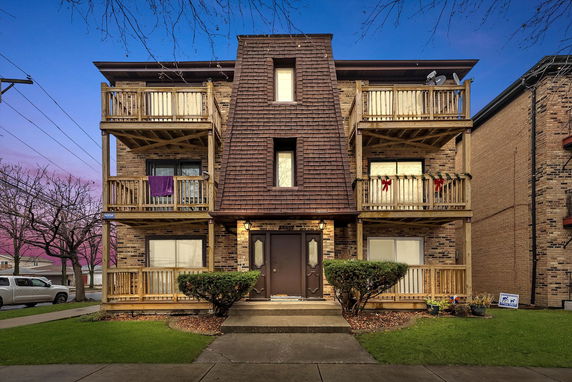Front view of a three-story apartment building with wooden balconies and a central entrance.