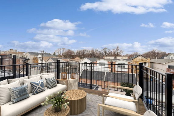 Panoramic view from a rooftop deck with outdoor seating and railings overlooking a residential area.