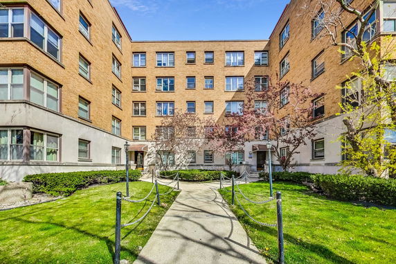 Front view of a multi-story apartment building with a pathway leading to the entrance.