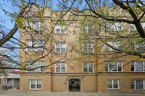 Front view of a multi-story brick apartment building with several windows and an arched entrance.
