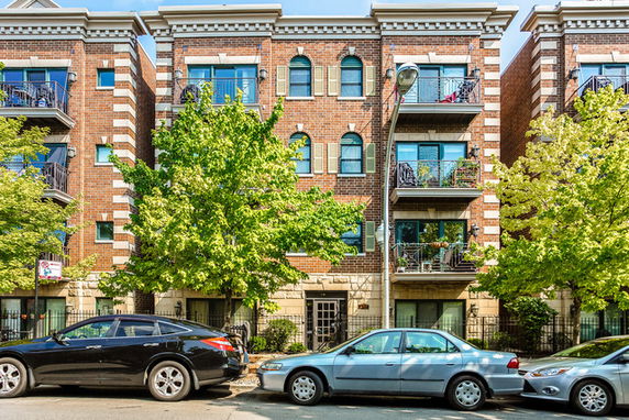 Front view of a multi-story brick apartment building with balconies and arched windows.