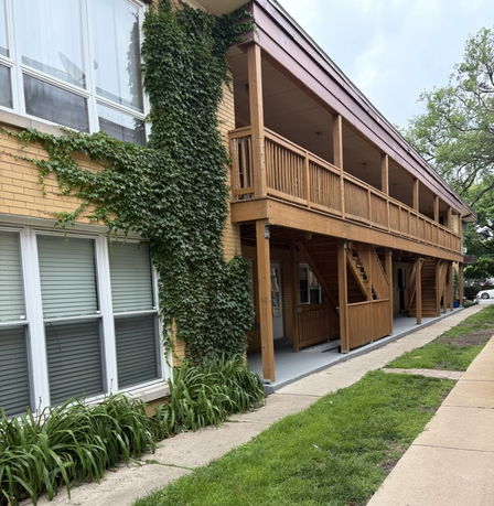Exterior view of a two-story building with ivy growing on brick walls and wooden balcony.