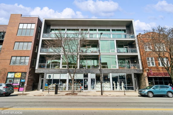 Front view of a modern multi-story building with large glass windows and retail space on the ground floor.
