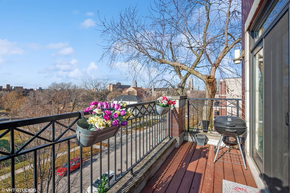 Panoramic view from a balcony overlooking tree-lined streets and distant buildings.