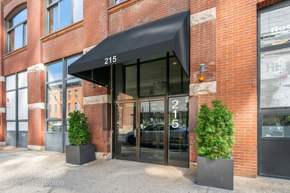 Front view of a brick building entrance with a black awning and glass doors.