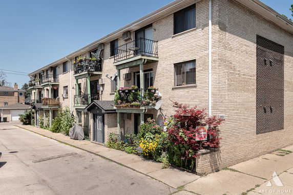 Front view of a multi-story apartment building with balconies and potted plants.