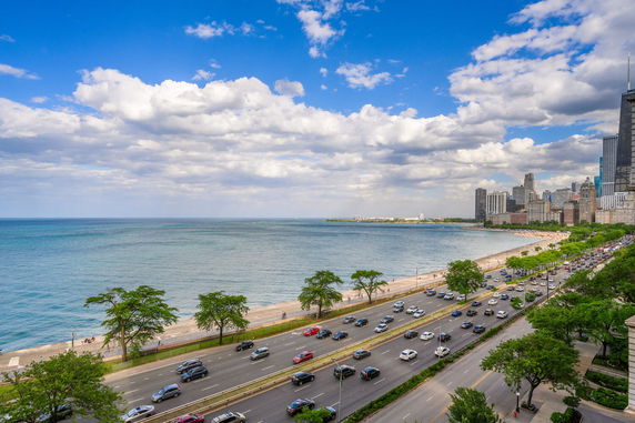 Panoramic view of a coastline with a busy road and city skyline in the background.