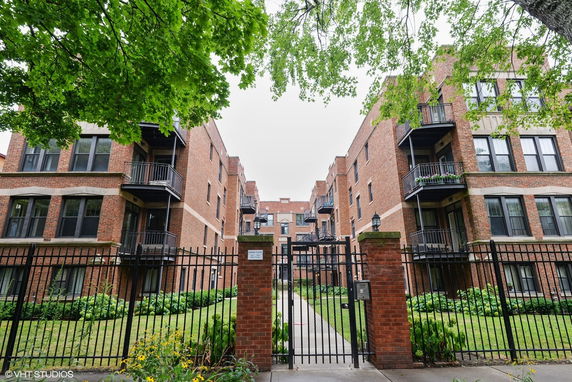 Front view of a multi-story brick apartment building with balconies and a gated entrance.