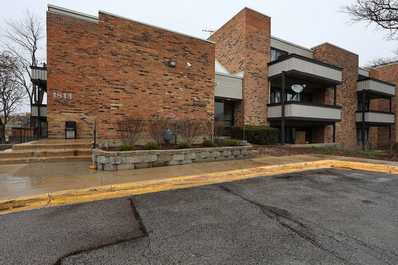 Front view of a multi-story brick apartment building with balconies and a visible entrance.