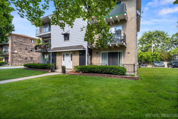 Front view of a multi-story residential building with balconies and a well-maintained lawn.