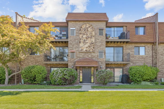 Front view of a three-story brick apartment building with balconies.
