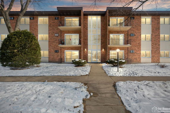 Front view of a three-story brick apartment building with balconies and central glass entrance.