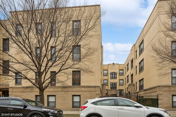 Front view of a multi-story brick building with parked cars and bare trees.