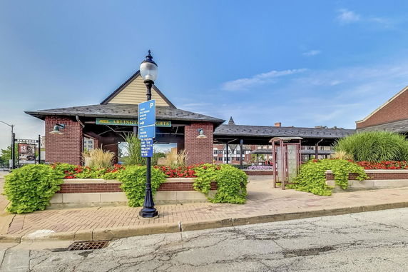 Front view of a building with a gabled roof and brick exterior, featuring signage and landscaped plants.