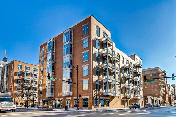Front view of a modern multi-story residential building on a street corner with large windows and balconies.