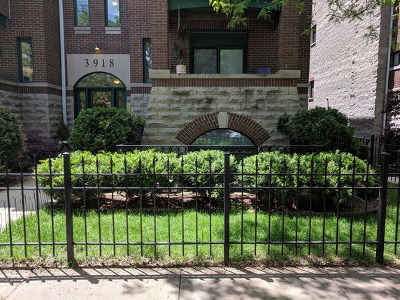 Front view of a brick building entrance with arched windows and a metal fence.