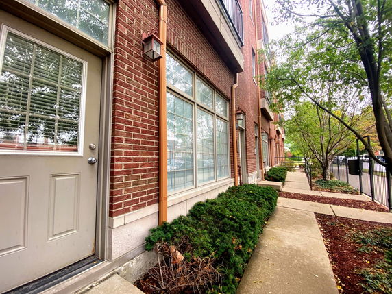 Front view of a brick townhouse with large windows and a path leading alongside it.