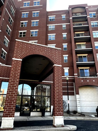 Front view of a multi-story brick apartment building with an arched entrance.