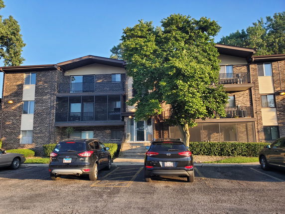 Front view of a multi-story apartment building with balconies and parking space in front.