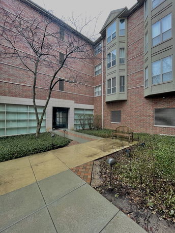 Front view of a multi-story brick building with large windows and a courtyard entrance.