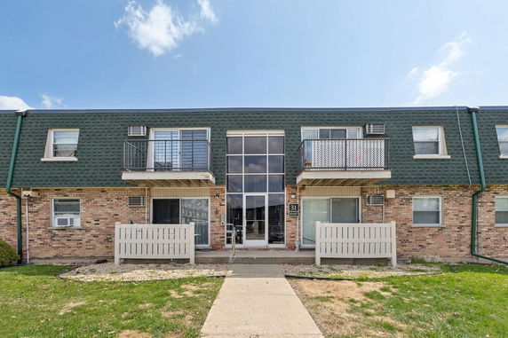 Front view of a two-story apartment building with a brick facade and green roof.