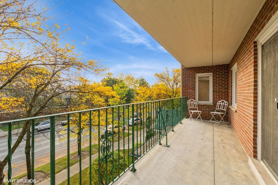 View from a balcony with metal railing overlooking a tree-lined street.