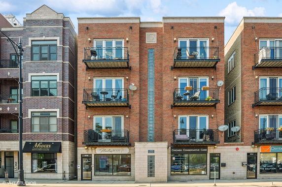 Front view of a multi-story brick building with balconies and retail shops at ground level.