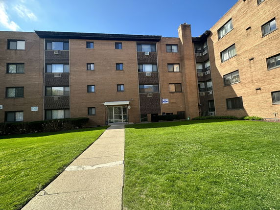 Front view of a multi-story apartment building with a pathway leading to the entrance.