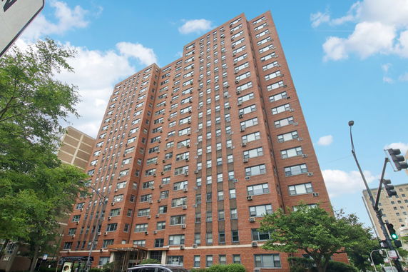 Front view of a high-rise brick apartment building with multiple windows and air conditioners.