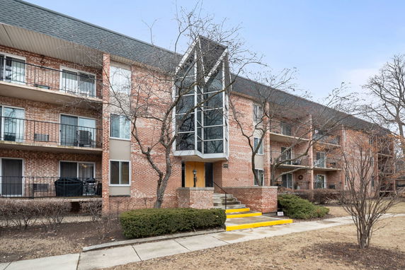 Front view of a multi-story apartment building with balconies and a central glass entrance.